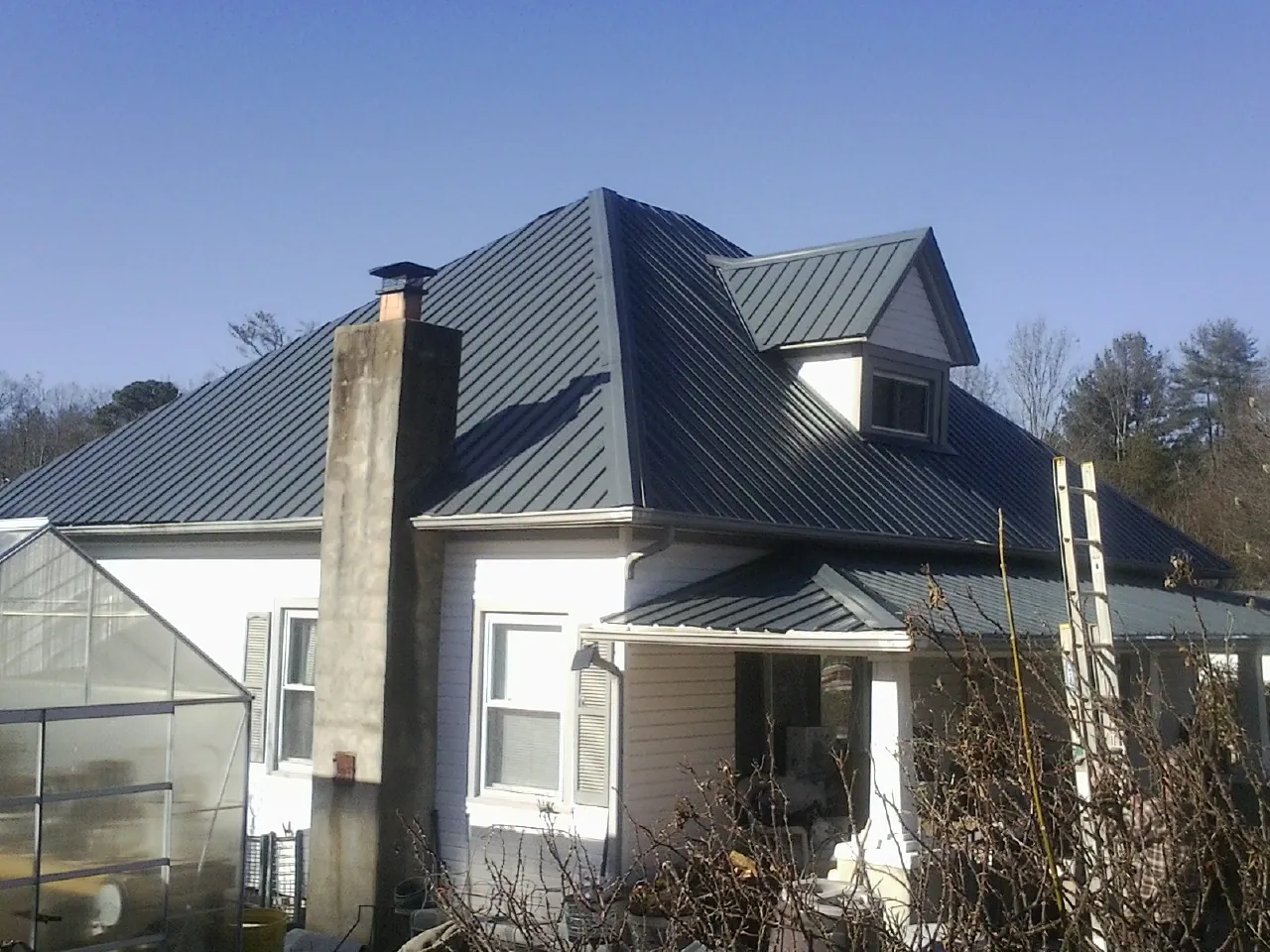 Dark blue standing seam metal roof on a white farmhouse with dormer — Slate & Tile Roof Repair by Roofing Brothers in Wirtz