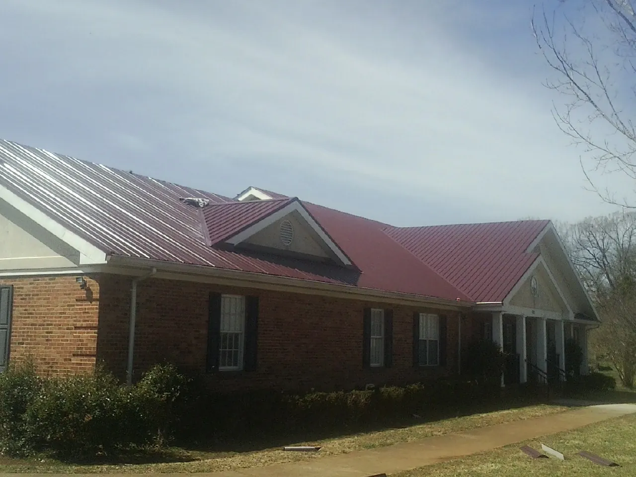Red metal roof with gabled entries on a long brick building, from a Hail Damage Roof Repair job in Wirtz