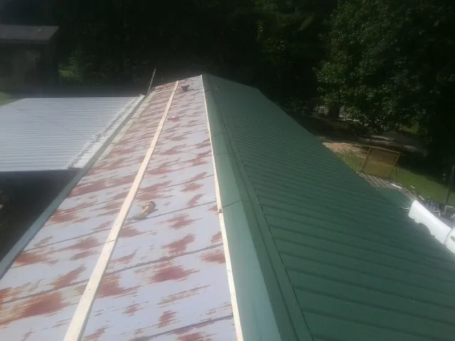 Old rusted panels beside newly installed green metal roofing — Wind Damage Roof Repair by Roofing Brothers in Wirtz