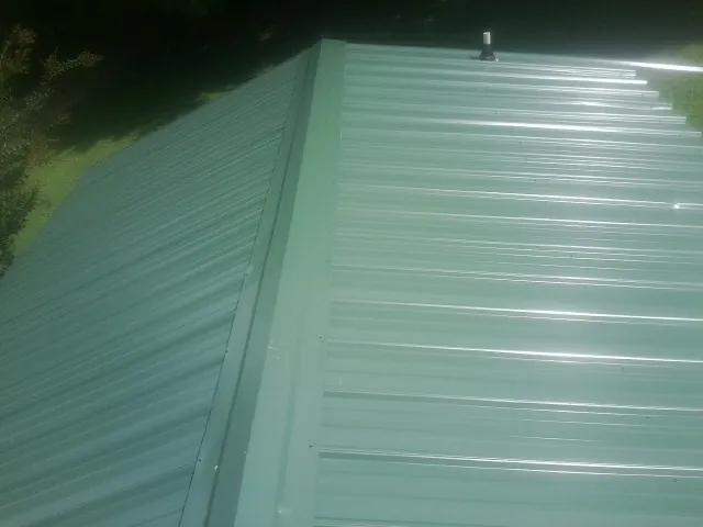 New green metal panels meeting at the ridge of a roof — Flat Roof Repair work by our crew in Wirtz