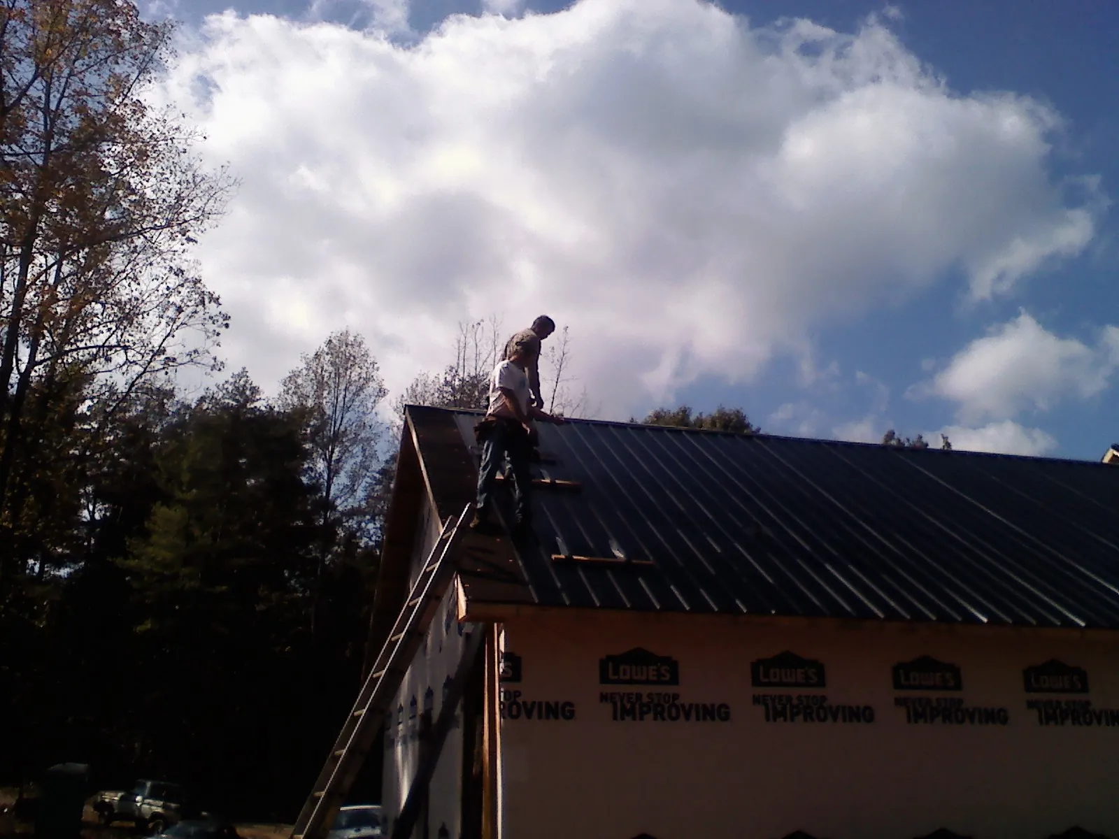 Roofer fastening dark metal panels high against a cloudy sky, from a Roof Inspection job in Wirtz