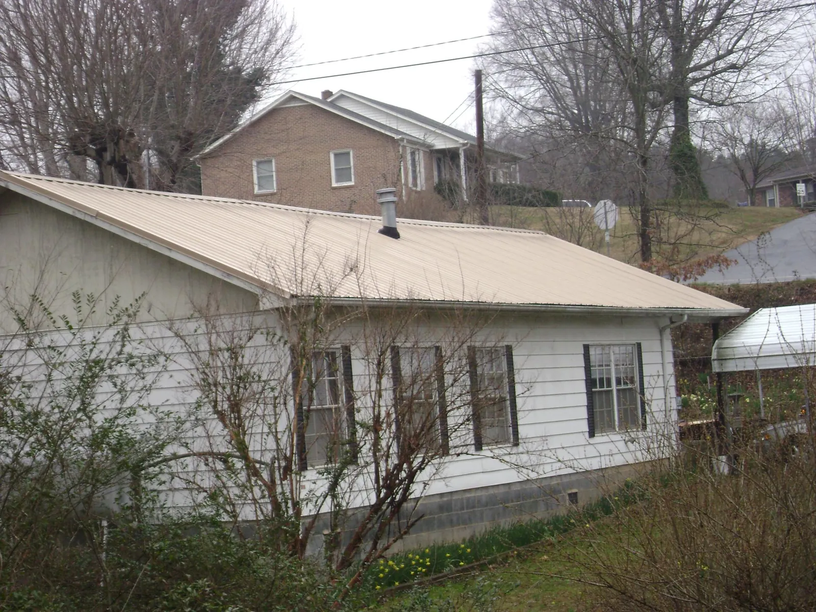Tan metal roof on a white sided house set into a hillside — Commercial Roofing by Roofing Brothers in Wirtz