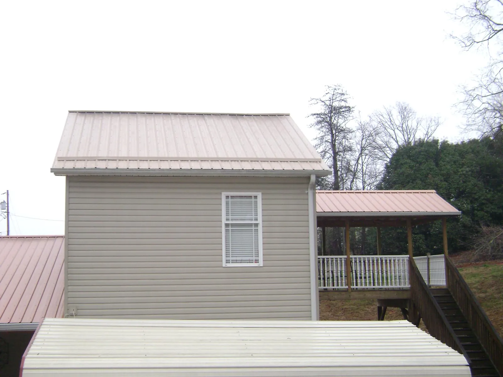 Tan metal roofs on a two story addition and attached porch, from a Roof Replacement job in Wirtz